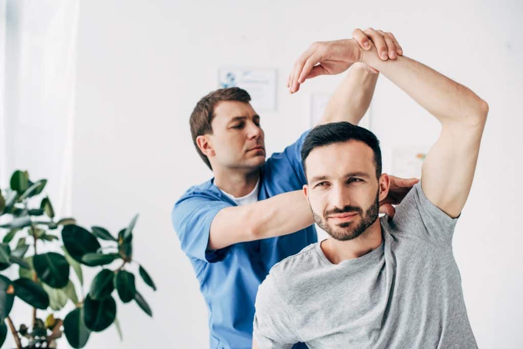 chiropractor stretching arm of handsome patient in hospital